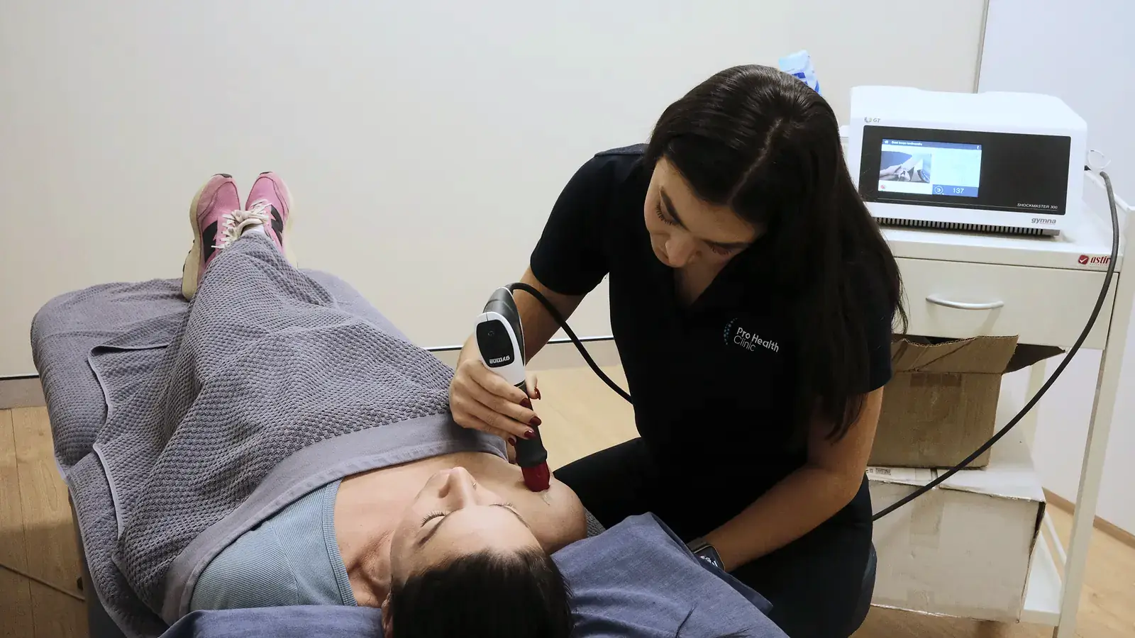 Shockwave therapy handpiece applied to a patient’s shoulder